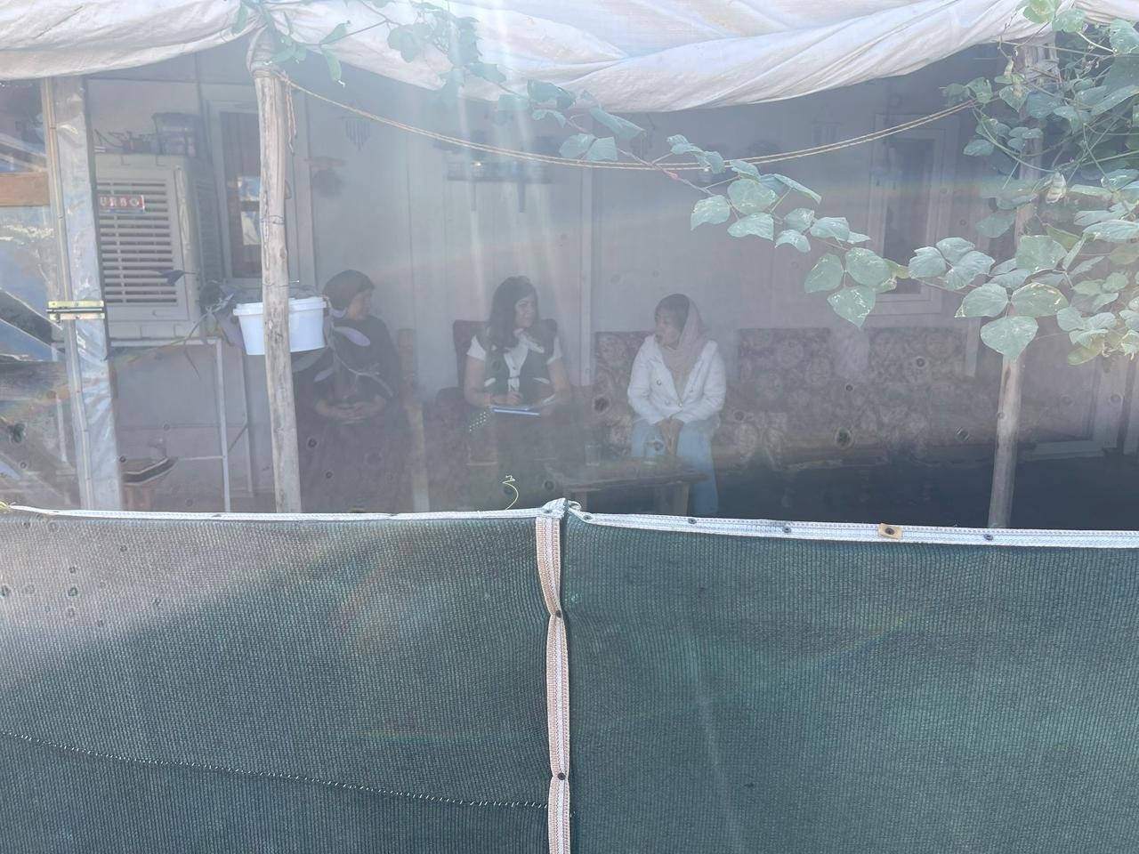 Three women seated together during a household interview in a camp shelter