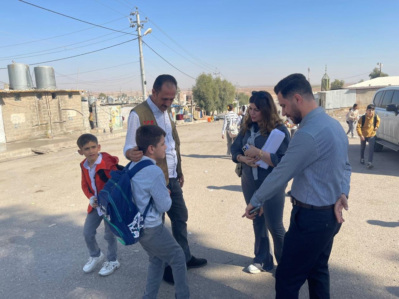 KIANO staff talking with a community worker and residents on a street in a displacement site near Duhok