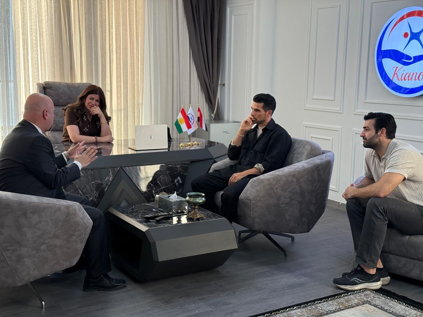 A meeting in the KIANO office in Duhok, with the organization's logo on the wall and Kurdistan and Iraq flags on the desk