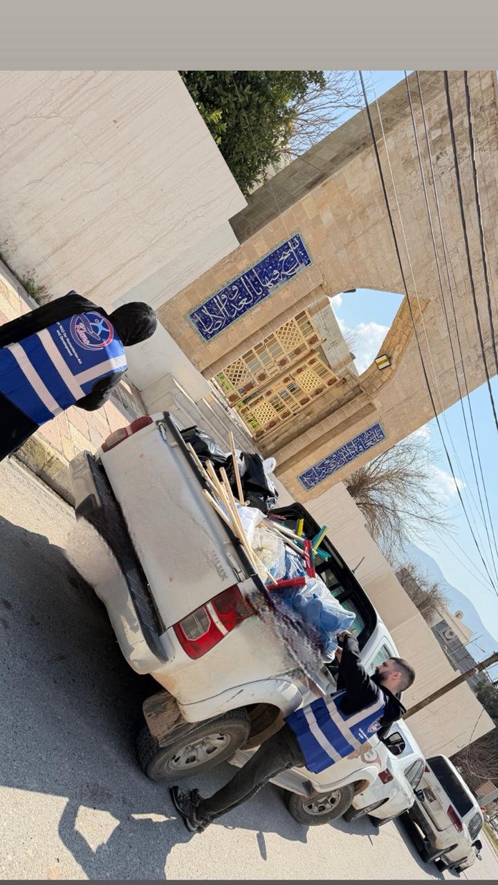 Brooms and cleaning supplies loaded into a pickup truck outside a mosque gate