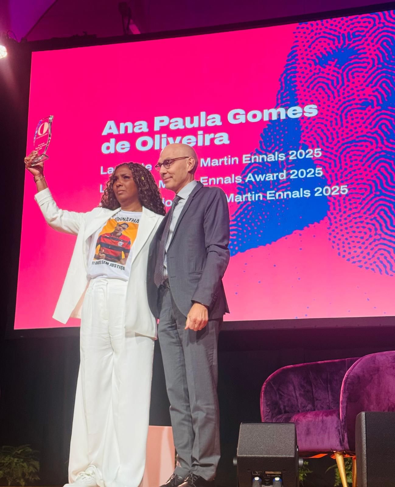 Martin Ennals Award 2025 ceremony, with laureate Ana Paula Gomes de Oliveira holding the award on stage
