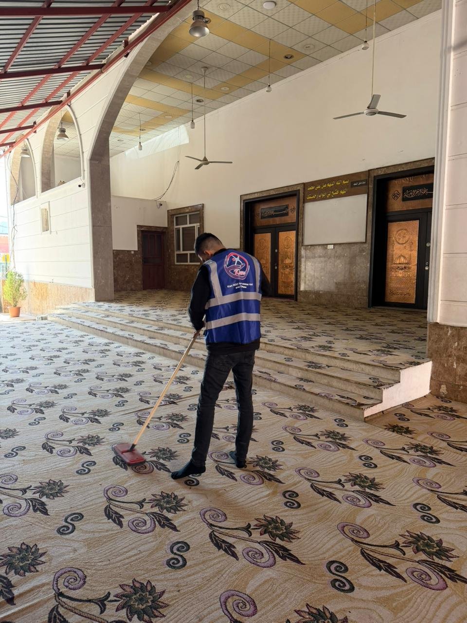 A volunteer sweeping the carpeted prayer hall of a mosque